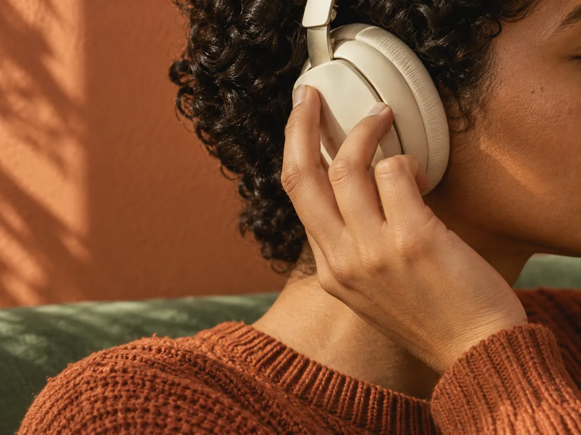 A close-up of a listener adjusting cream headphones while reviewing a recording